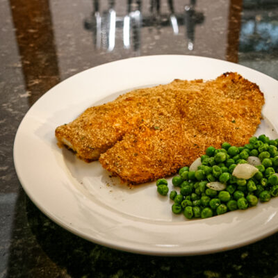 A plate with oven-fried tilapia and peas.