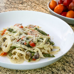 a bowl of pasta with asparagus and ham in a parmesan cheese sauce