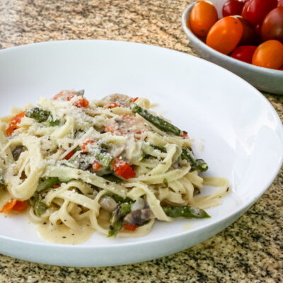 a bowl of pasta with asparagus and ham in a parmesan cheese sauce