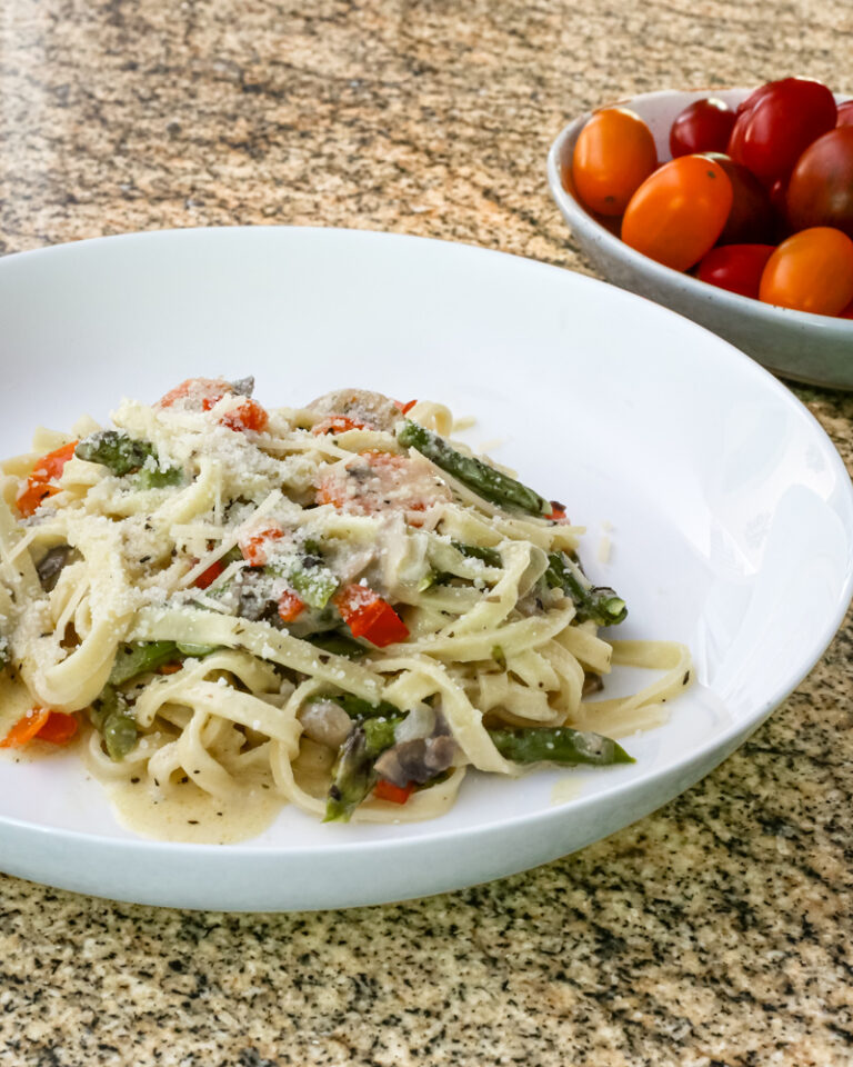 a bowl of pasta with asparagus and ham in a parmesan cheese sauce
