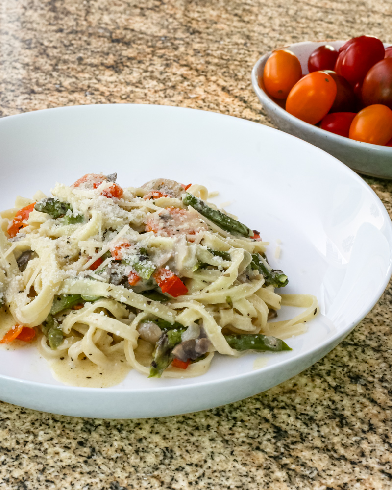 a bowl of pasta with asparagus and ham in a parmesan cheese sauce