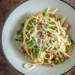 pasta with pancetta and peas on a plate with pecorino romano cheese garnish