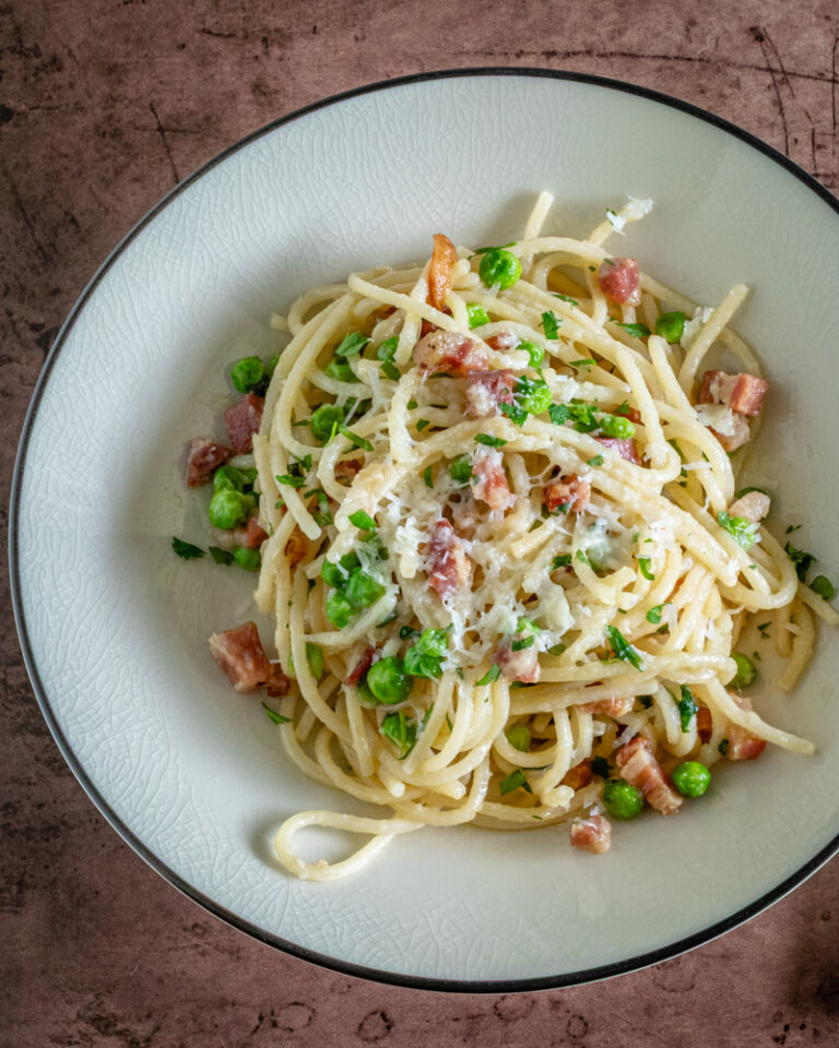 pasta with pancetta and peas on a plate with pecorino romano cheese garnish