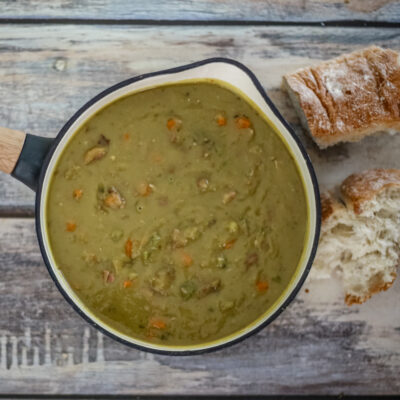 A saucepan with pea soup and crusty bread on the side