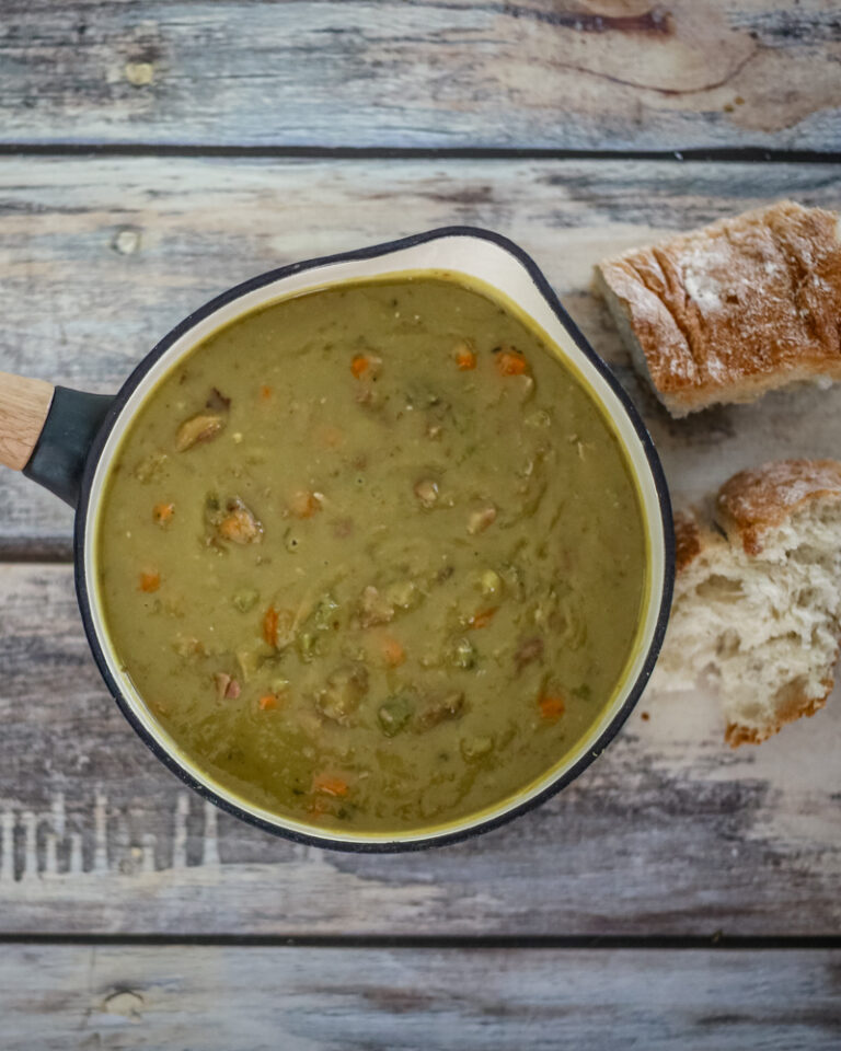 A saucepan with pea soup and crusty bread on the side