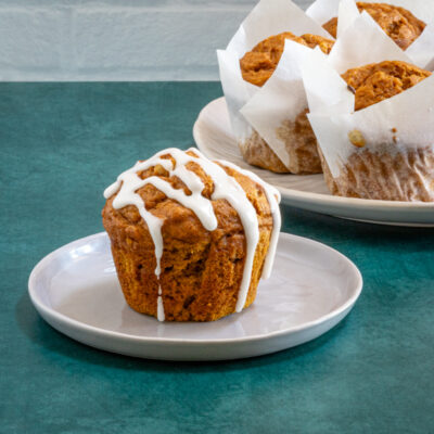 Golden brown muffin topped with white icing on a small white plate.