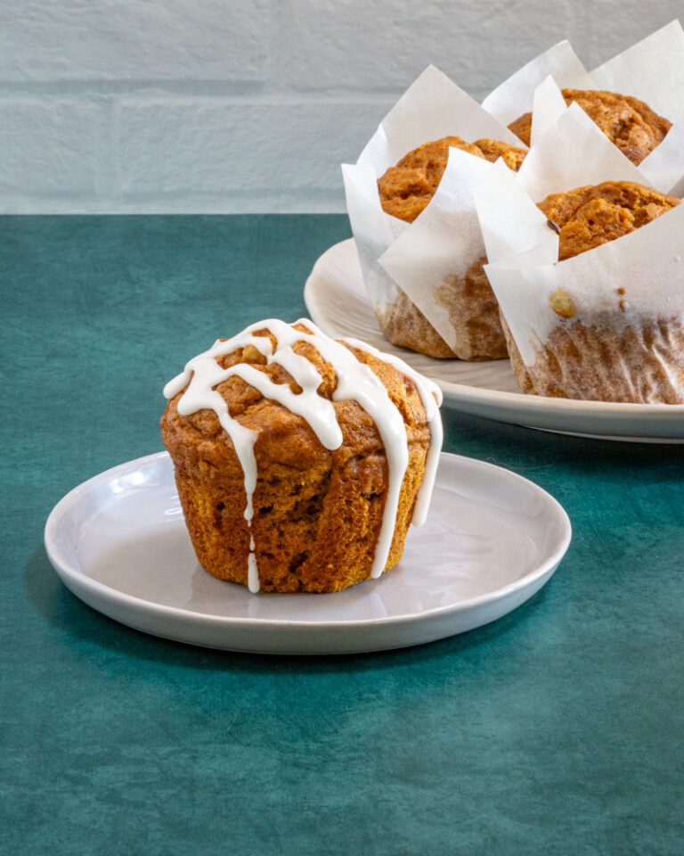Golden brown muffin topped with white icing on a small white plate.