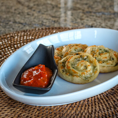 crescent pesto pinwheel snack on a plate, with marinara sauce.