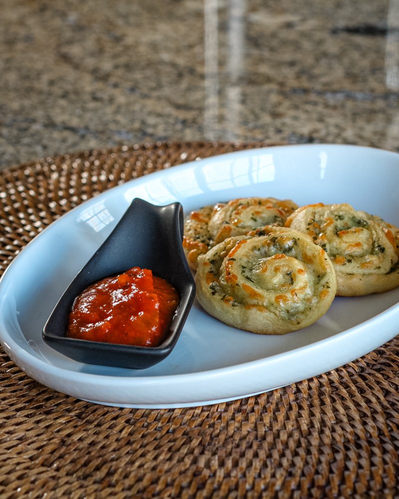 crescent pesto pinwheel snack on a plate, with marinara sauce.
