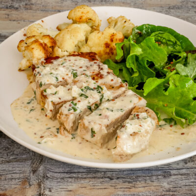 pork chops with mustard cream sauce on a plate with cauliflower and salad