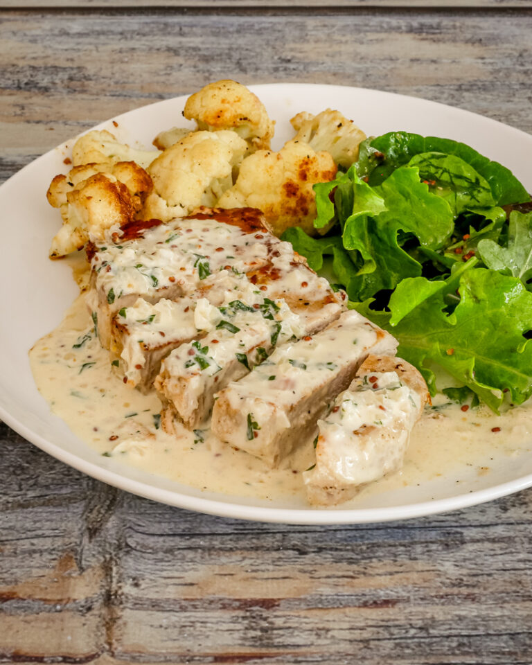 pork chops with mustard cream sauce on a plate with cauliflower and salad