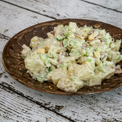 A bacon and egg potato salad on a serving plate with some sliced hard-boiled eggs on the side.