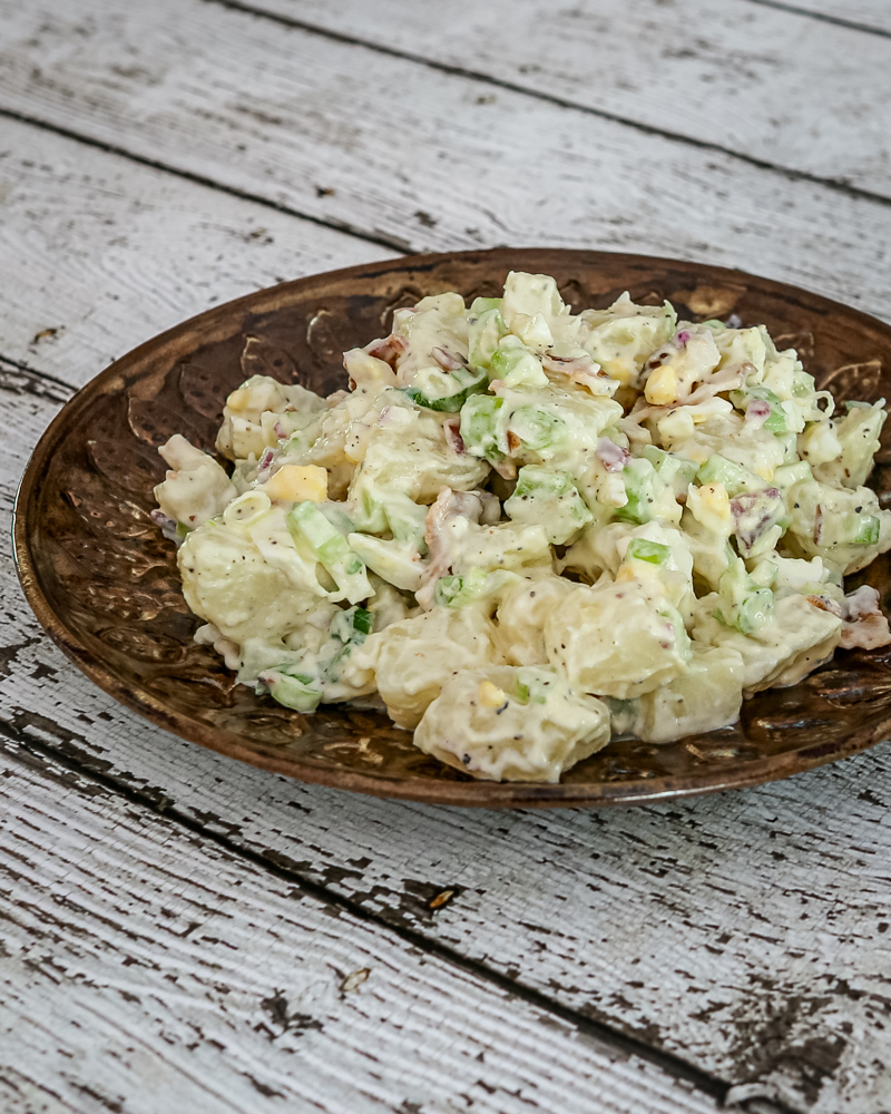 A bacon and egg potato salad on a serving plate with some sliced hard-boiled eggs on the side.