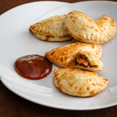 Pulled pork empanadas on a serving plate with bbq sauce.