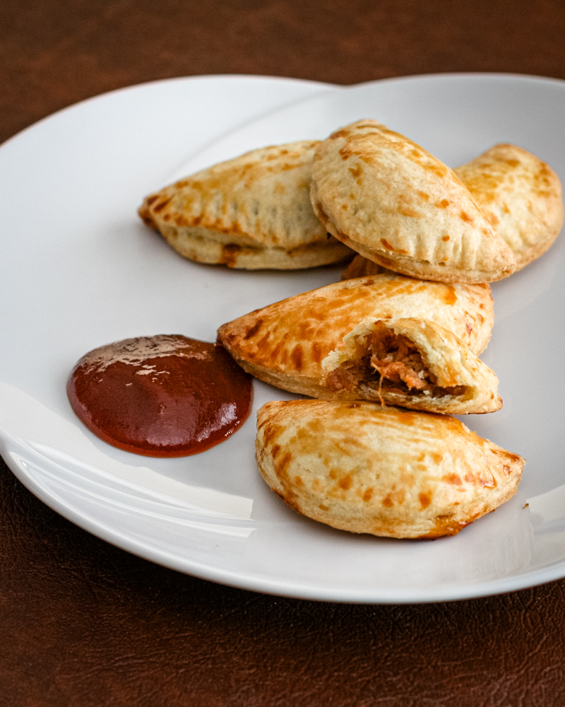 Pulled pork empanadas on a serving plate with bbq sauce.