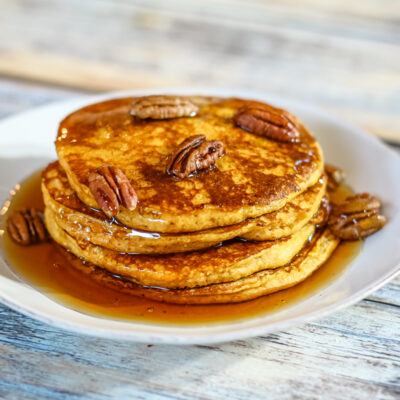 A stack of pumpkin pancakes with toasted pecans and syrup.