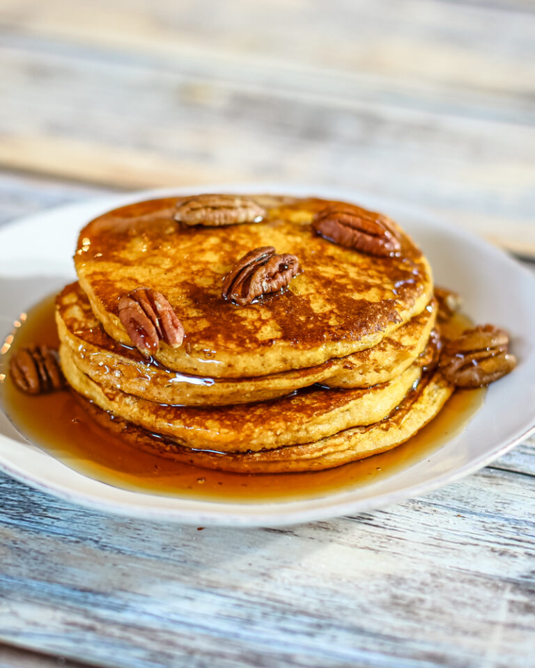 A stack of pumpkin pancakes with toasted pecans and syrup.