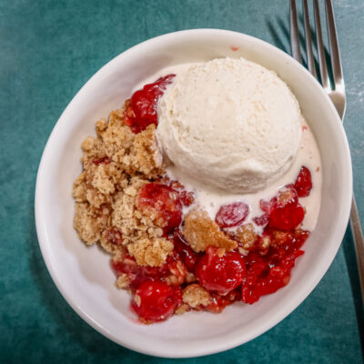an easy cherry crisp in a dessert dish with a scoop of ice cream