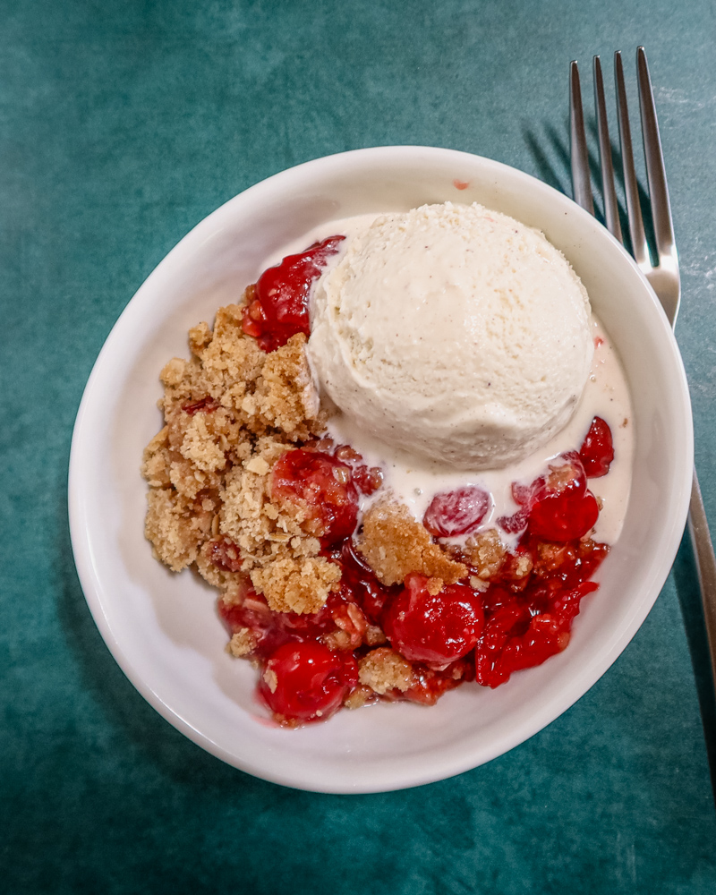 an easy cherry crisp in a dessert dish with a scoop of ice cream