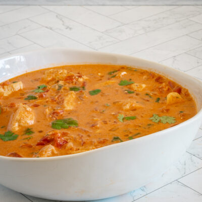 A serving bowl of coconut curry chicken with cilantro garnish.