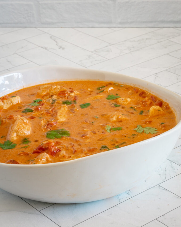 A serving bowl of coconut curry chicken with cilantro garnish.
