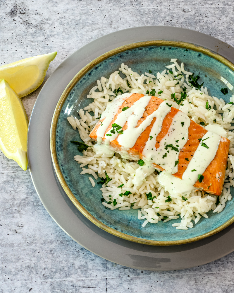 a salmon fillet on a bed of rice with a drizzle of basil mayonnaise.