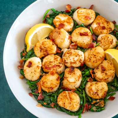 scallops on a bed of spinach with lemon wedges and bits of bacon