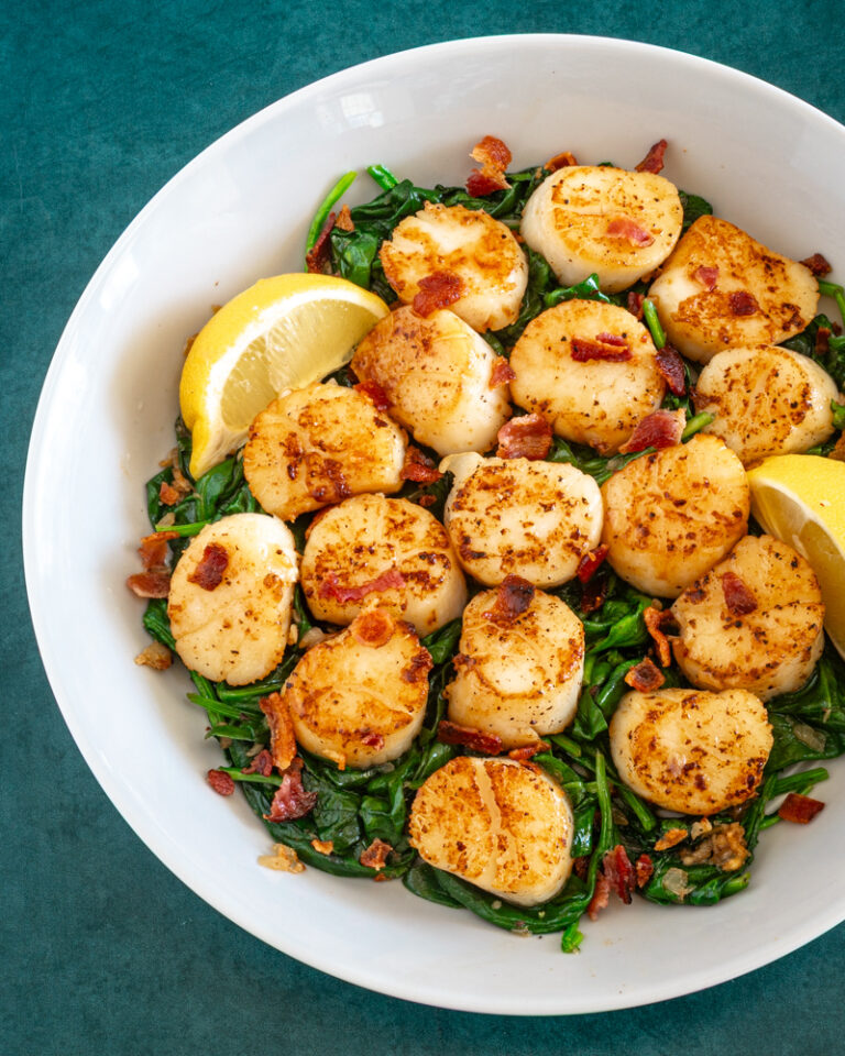 scallops on a bed of spinach with lemon wedges and bits of bacon