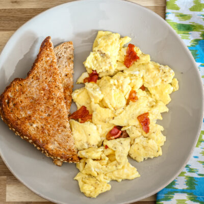 A plate of scrambled eggs with bacon and slices of toast on the side