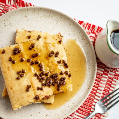 Slices of sheet pan pancakes on a plate with chocolate chip topping and syrup on the side.