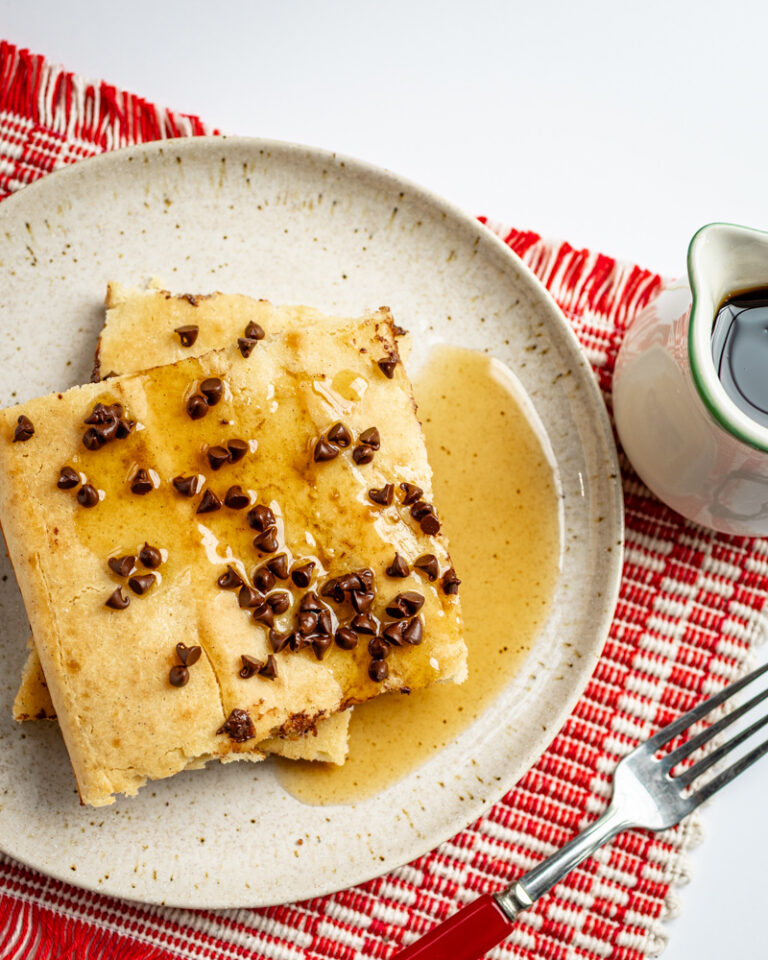 Slices of sheet pan pancakes on a plate with chocolate chip topping and syrup on the side.