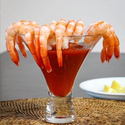 Succulent shrimp hanging on the rim of a cocktail glass filled with a red drink.