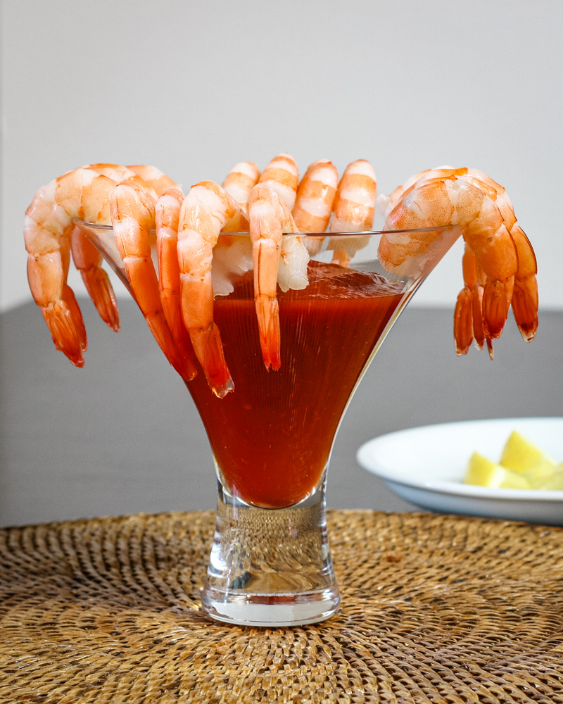 Succulent shrimp hanging on the rim of a cocktail glass filled with a red drink.