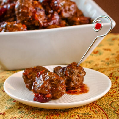 slow cooker cranberry meatballs appetizer in a white dish with a decorative metal appetizer pick.