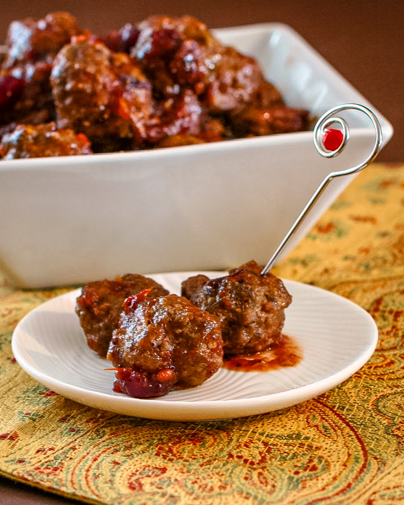 slow cooker cranberry meatballs appetizer in a white dish with a decorative metal appetizer pick.