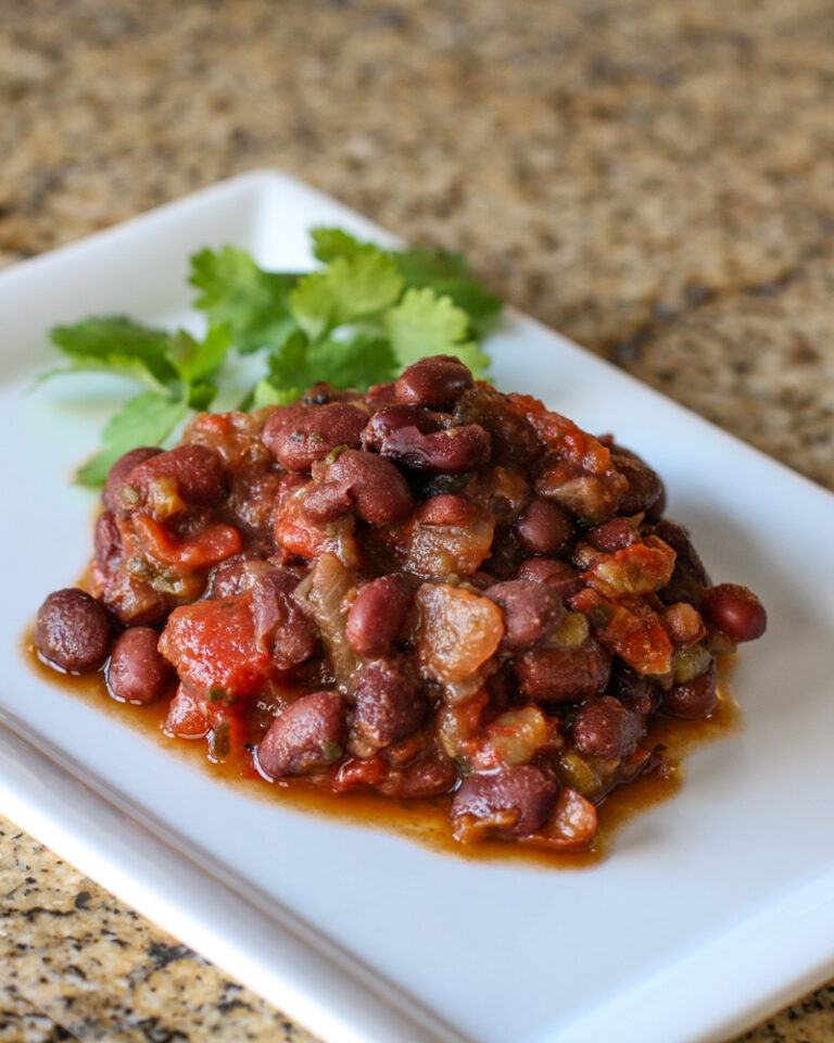 Tex Mex black beans and tomatoes on a plate with cilantro leaves.