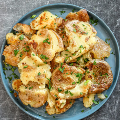 Fried smashed potatoes on a plate with parsley garnish.