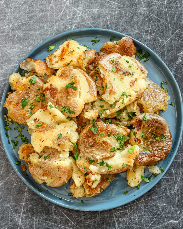 Fried smashed potatoes on a plate with parsley garnish.