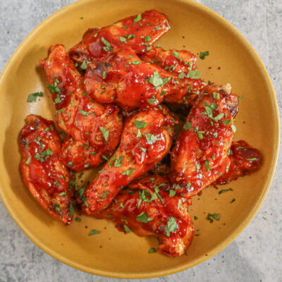 A serving bowl with air fryer Korean chicken wings in spicy sauce with cilantro and gochugaru garnish.