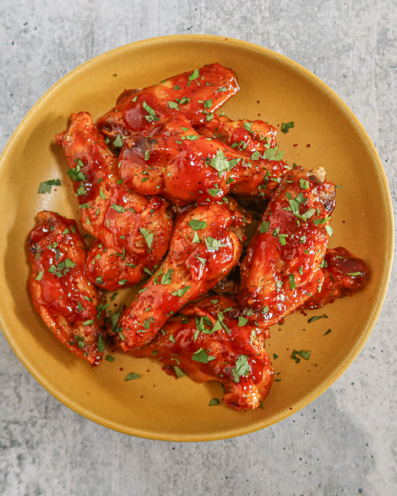 A serving bowl with air fryer Korean chicken wings in spicy sauce with cilantro and gochugaru garnish.