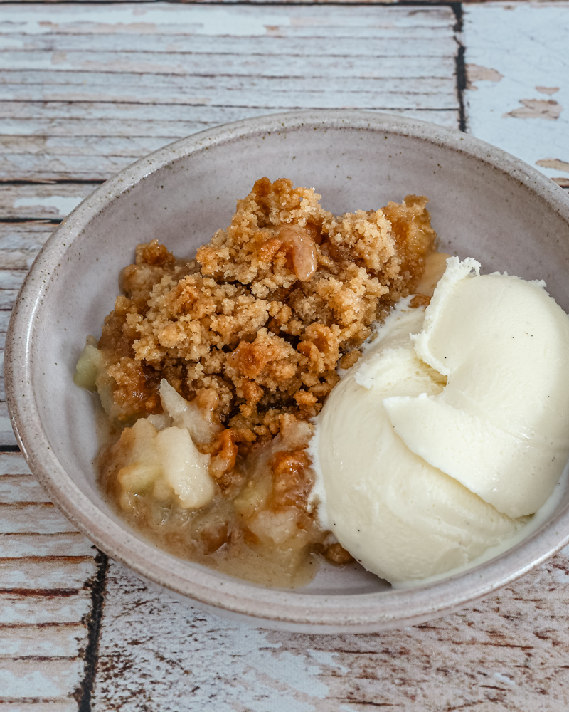 An apple crumble dessert in a small bowl with vanilla ice cream.