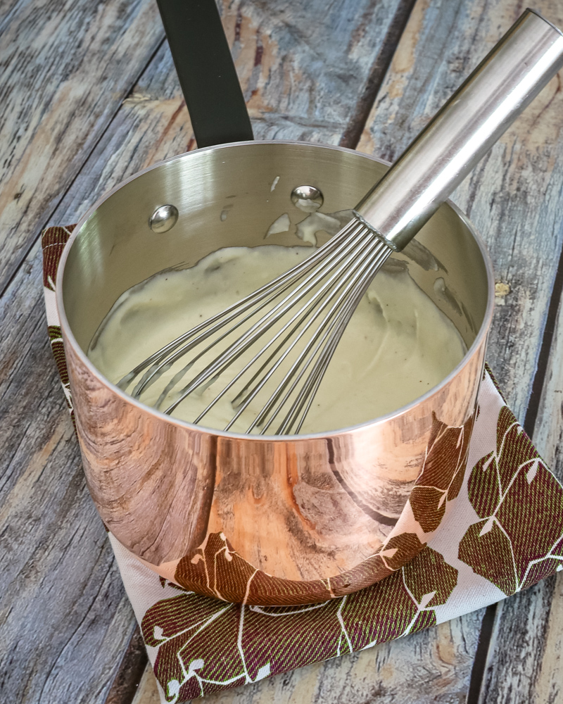A pan of cheese sauce with a whisk.