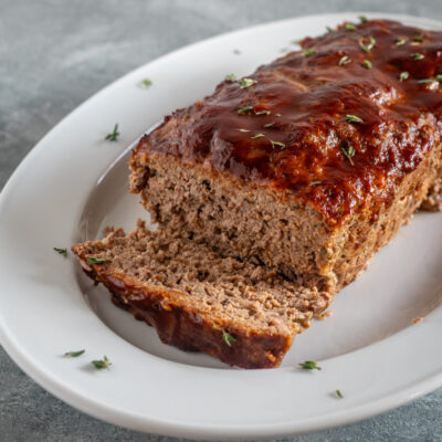 a meatloaf with BBQ glaze, sliced on a white platter.