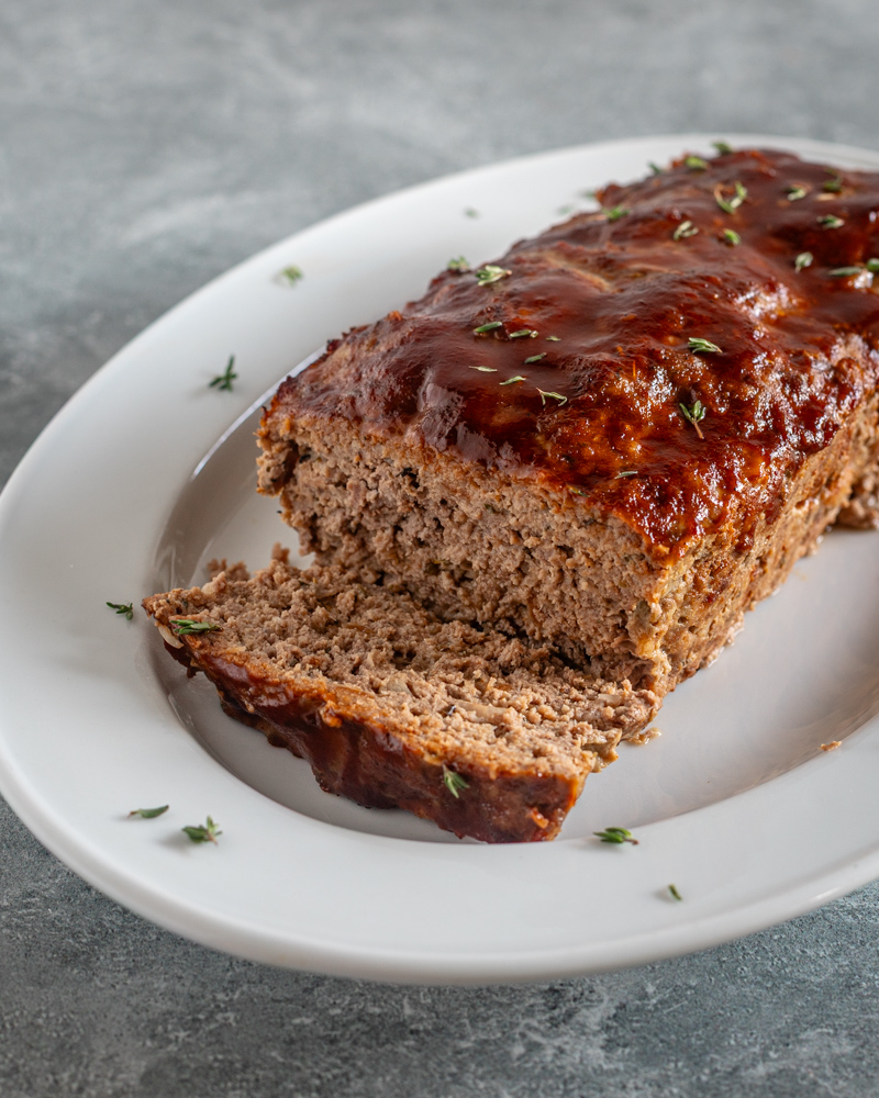 a meatloaf with BBQ glaze, sliced on a white platter.