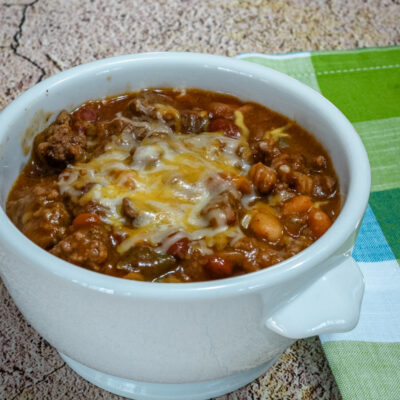 beef and beans with cheese in a bowl with napkin on the side