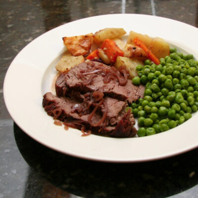 Roast beef with vegetables and green peas on white plate.