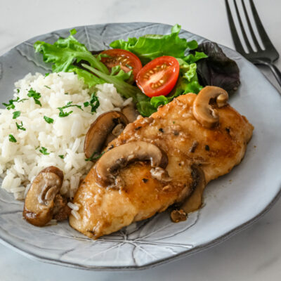 Chicken marsala on a gray plate with mushrooms and rice on the side.