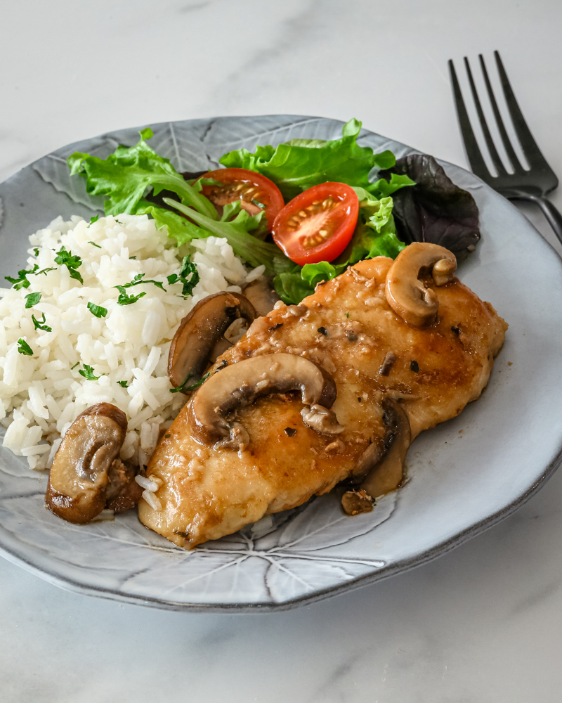 Chicken marsala on a gray plate with mushrooms and rice on the side.