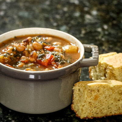 black-eyed pea soup with tomatoes and greens in a small cocotte with cornbread on the side