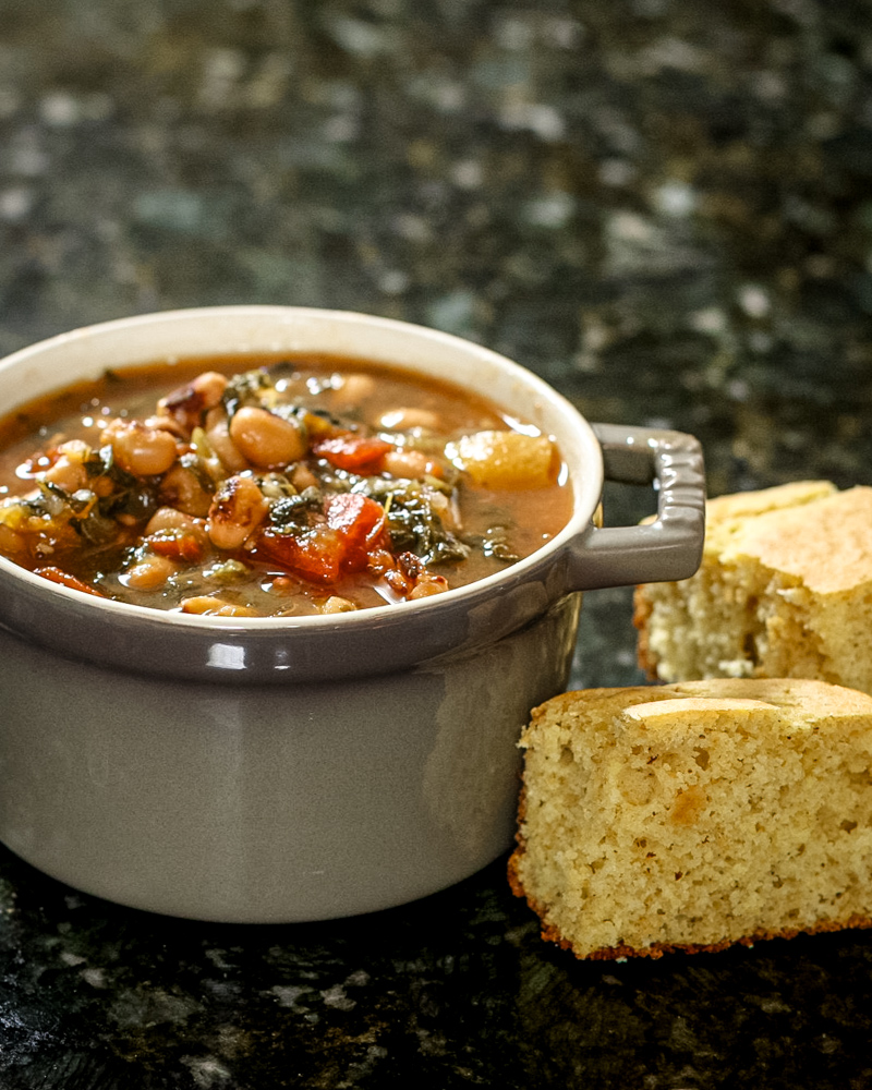 black-eyed pea soup with tomatoes and greens in a small cocotte with cornbread on the side